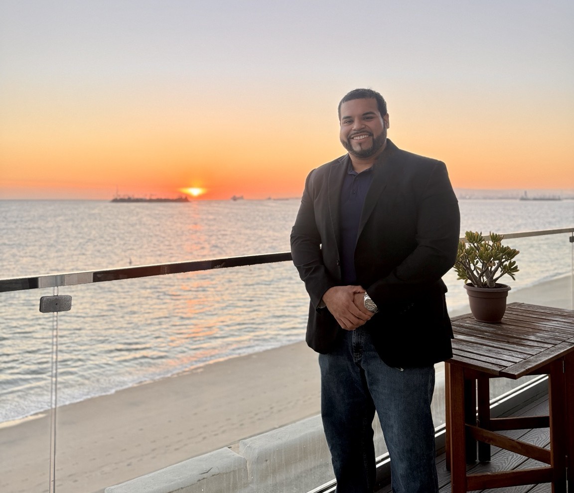 Manuel "Manny" Caballero, Founder & Principal Consultant at Caballero's Consulting, photographed at sunset on a waterfront terrace